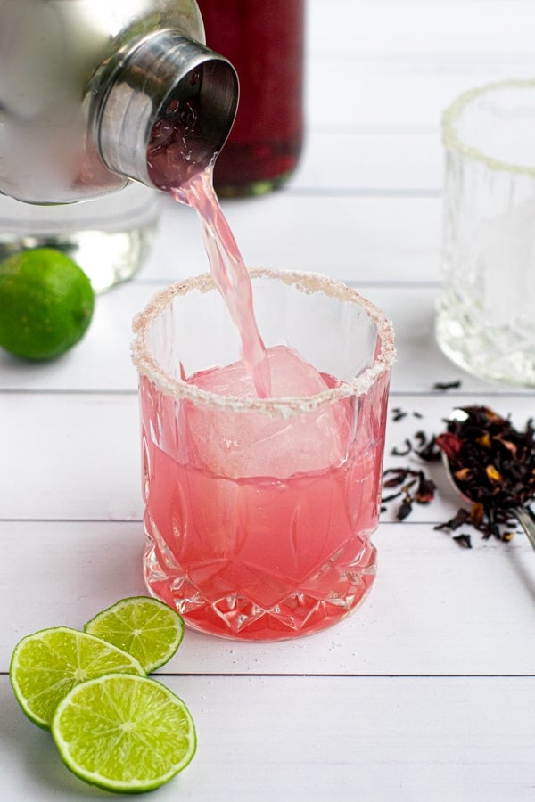 pink hibiscus margarita being poured from a cocktail shaker into a salt-rimmed glass
