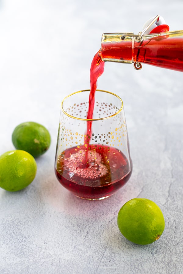 iced hibiscus tea being poured from a bottle into an empty glass