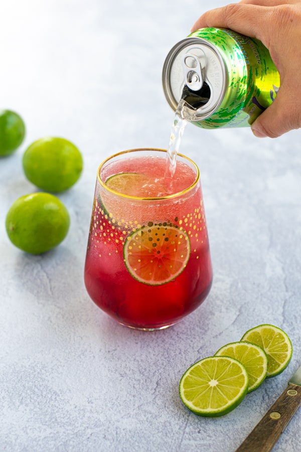 pouring a lime seltzer from a can into a glass half full of hibiscus tea