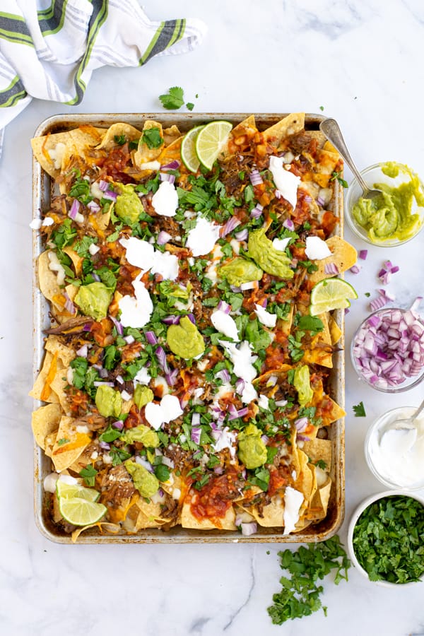 sheet pan full of nachos with carnitas, cheese, and toppings