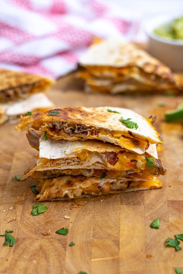 stack of 3 carnitas quesadillas on a wooden cutting board