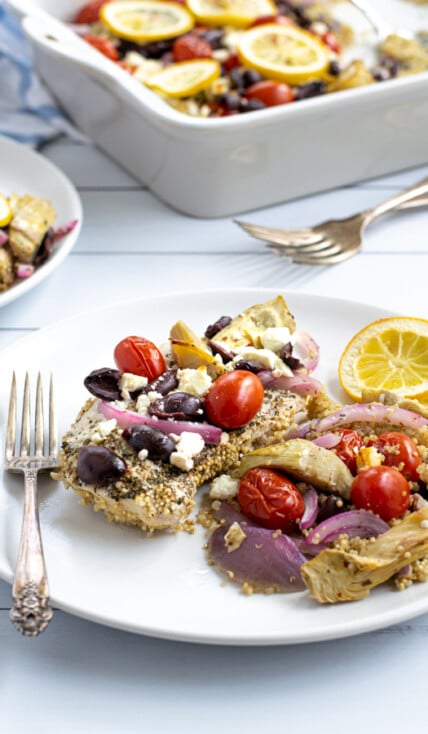 a baked greek chicken breast on a plate with greek toppings and quinoa