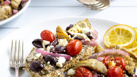 a baked greek chicken breast on a plate with greek toppings and quinoa
