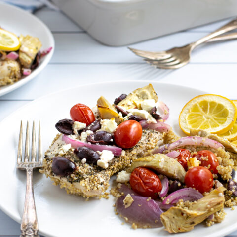 a baked greek chicken breast on a plate with greek toppings and quinoa