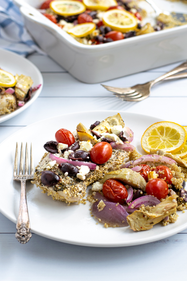 a baked greek chicken breast on a plate with greek toppings and quinoa