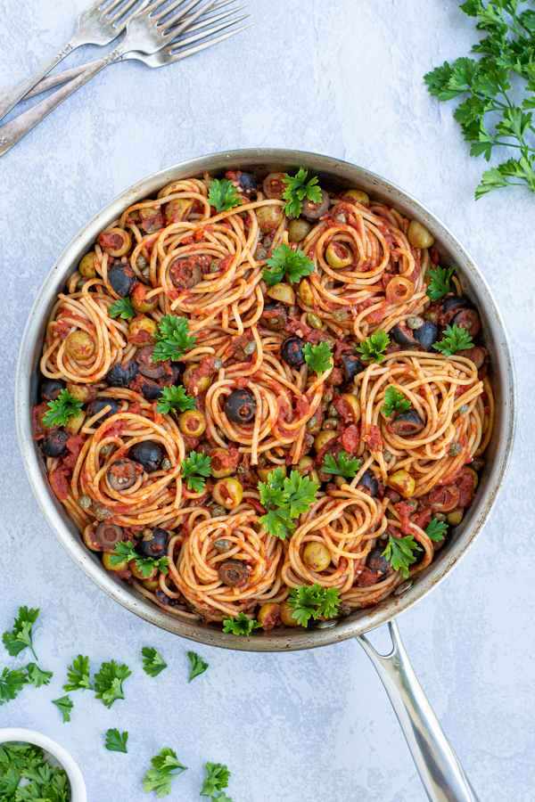 a large skillet with spaghetti Puttanesca garnished with parsley