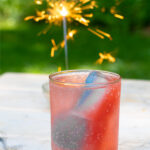 Pinterest Pin for red, white, and blue ice cubes showing a drink with patriotic ice cubes outside next to a sparkler