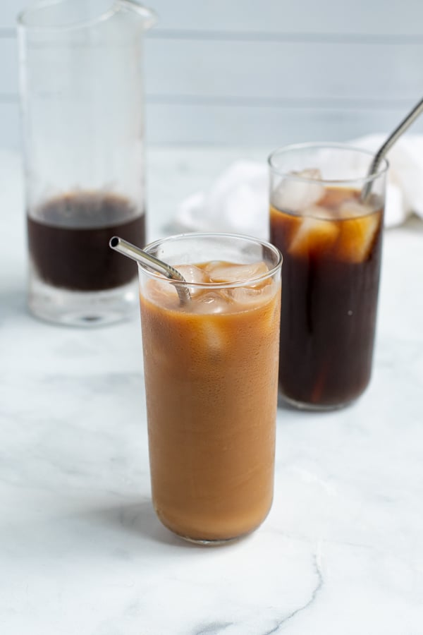 in the front a glass of cold brew coffee mix with milk next to a glass of plain cold brew coffee behind it