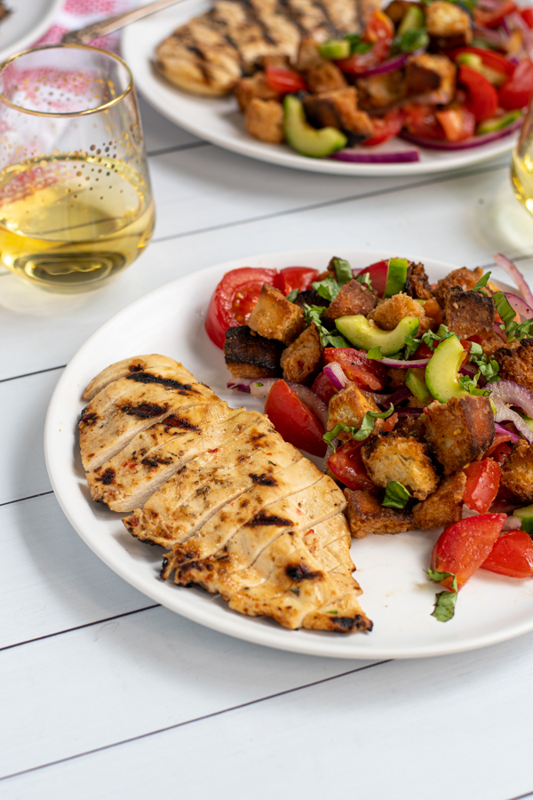 grilled chicken sliced up on a plate next to a large serving of panzanella salad with grilled bread