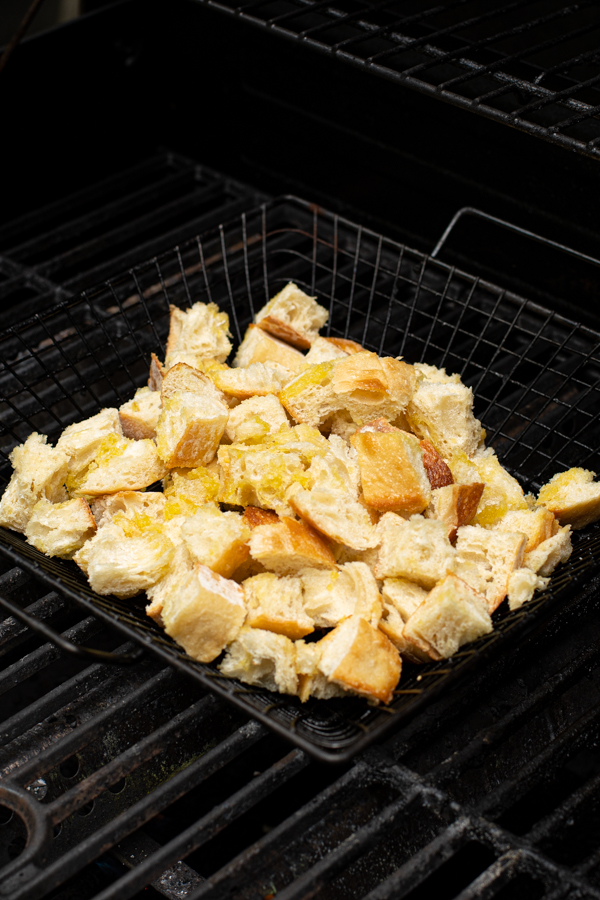 1 inch cubes of crusty bread in a grilling basket on the grill