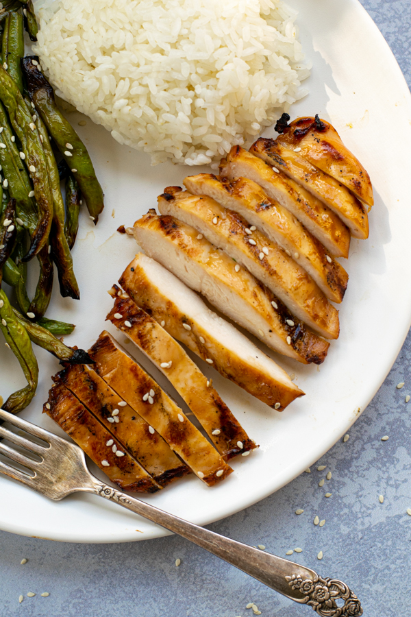 close up of a sliced up grilled chicken breast on a plate next to green beans and white rice