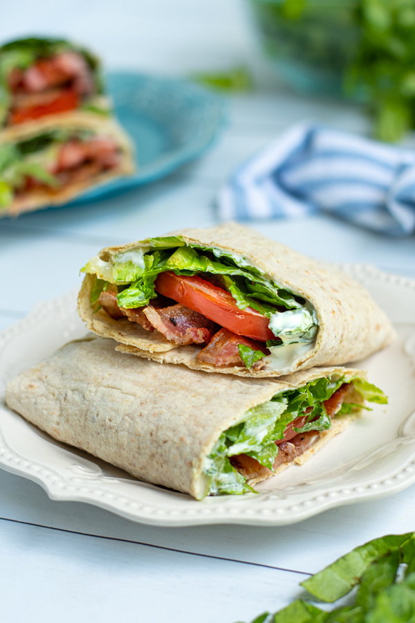 two halves of a BLT wrap on a white plate showing off the bacon, lettuce, tomato, and sauce on the inside