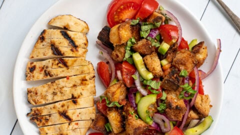 a white plate shot from overhead with sliced grilled chicken breast and a large serving of panzanella salad with tomatoes and grilled bread