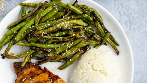 Overhead shot of a white plate with a teriyaki grilled chicken breast, grilled green beans with sauce, and white rice
