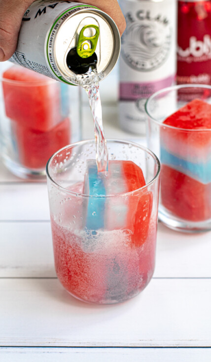 a glass with two red, white, and blue layered ice cubes with a hard seltzer being poured over top