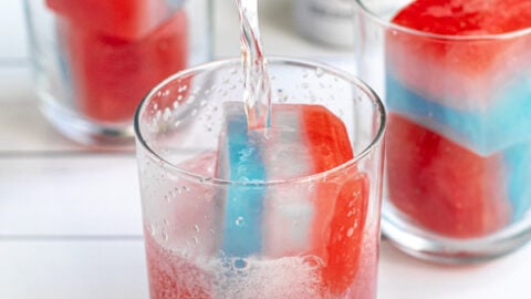 a glass with two red, white, and blue layered ice cubes with a hard seltzer being poured over top