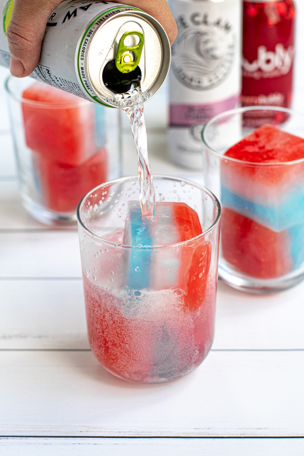 a glass with two red, white, and blue layered ice cubes with a hard seltzer being poured over top
