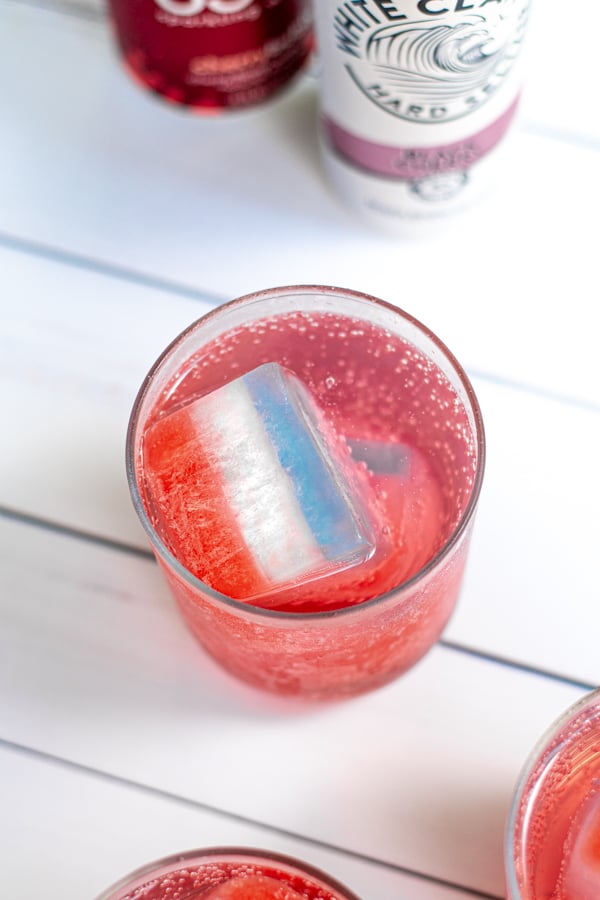 a layered red, white, and blue ice cube floating in a glass filled with a clear bubbly beverage