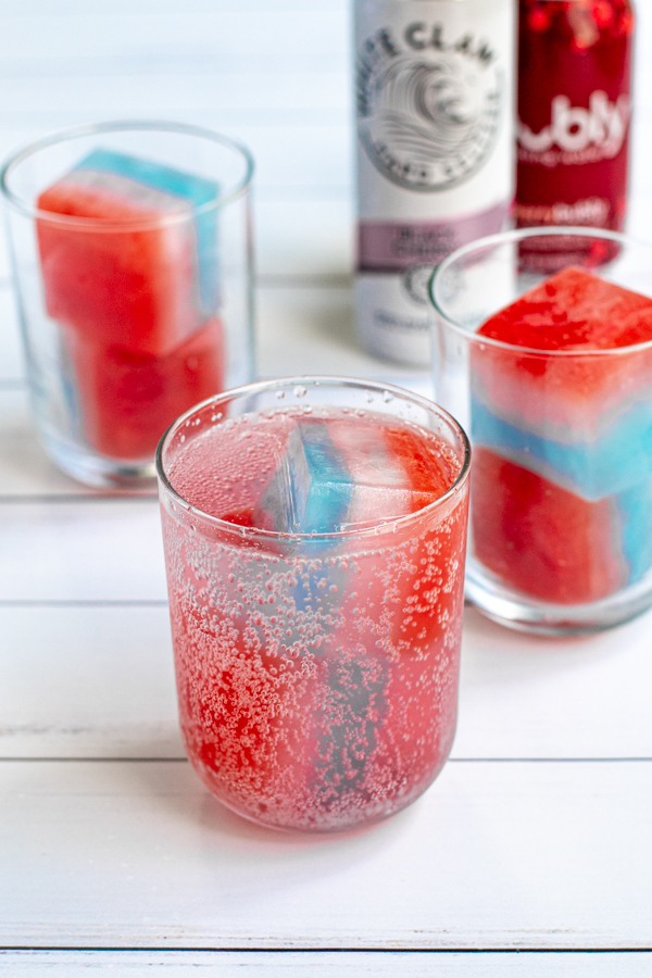a glass filled with freshly poured seltzer filled with res, white, and blue ice cubes