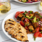 Pinterest Pin for Grilled Chicken Panzanella Salad showing a white plate with a grilled chicken breast and a pile of panzanella salad