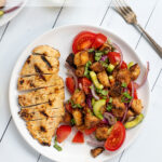 Pinterest Pin for Grilled Chicken Panzanella Salad showing a white plate with a grilled chicken breast and a pile of panzanella salad