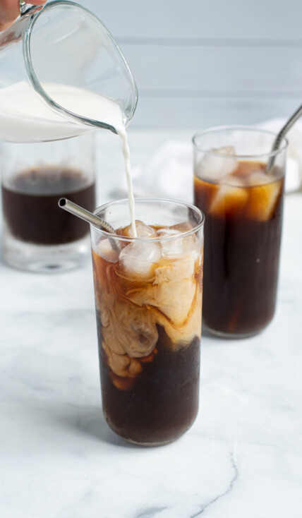 milk being poured into a glass of homemade cold brew coffee making milk and coffee swirls in the glass
