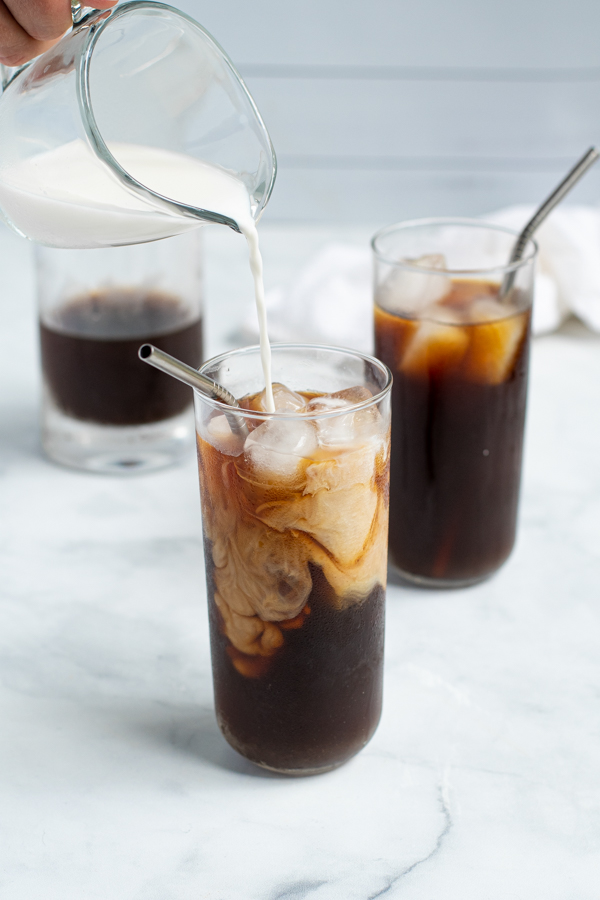 milk being poured into a glass of homemade cold brew coffee making milk and coffee swirls in the glass