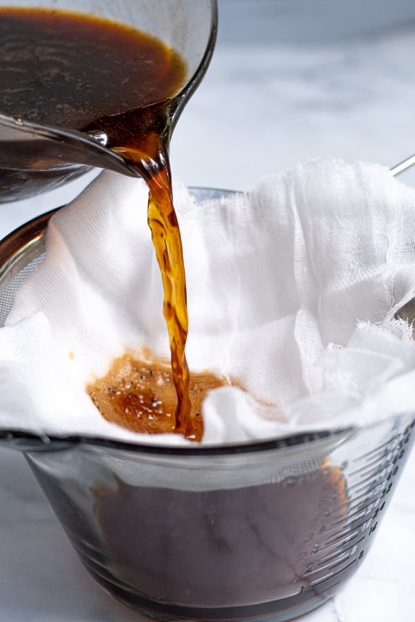 Pouring coffee concentrate and the used coffee grounds into a cheese cloth to strain out the coffee grounds