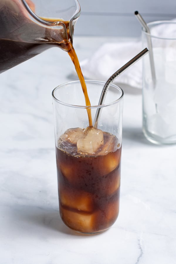 Pouring cold brew concentrate into a glass with ice cubes