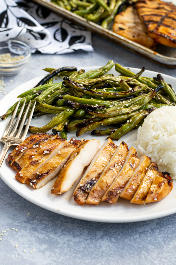 sliced grilled teriyaki chicken breast on a plate with crispy green beans and white rice