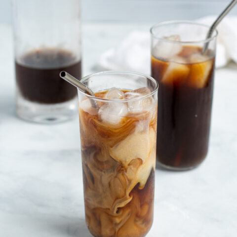 glass of homemade cold brew coffee with swirls of freshly poured milk with a straw and ice