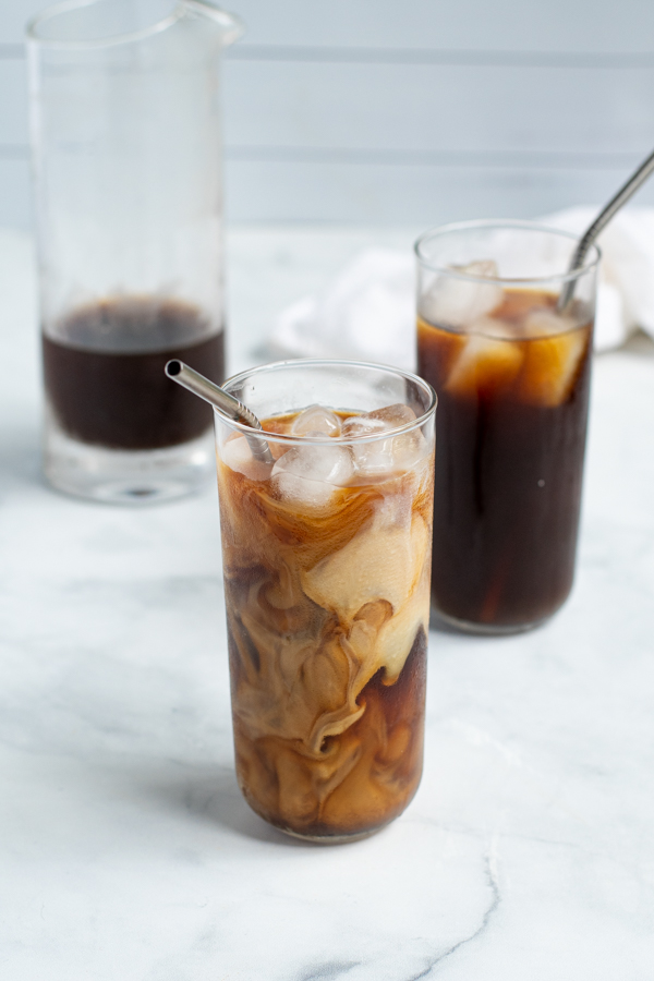 glass of homemade cold brew coffee with swirls of freshly poured milk with a straw and ice