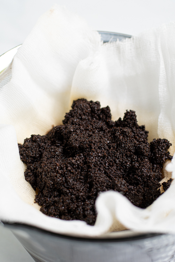 cheese cloth in a mesh strainer filled with used coffee grounds