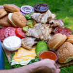 Pinterest Pin for Grilled Chicken Sandwich Board showing a man holding the large platter filled with chicken sandwich Ideas outside in the grass