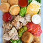 Pinterest Pin for Grilled Chicken Sandwich Board showing an overhead view of a large bamboo board containing grilled chicken, toppings, and buns
