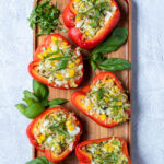 Pinterest Pin for Grilled Stuffed Bell Peppers showing five stuffed peppers arranged on a wooden tray next to fresh basil leaves