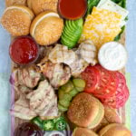 grilled chicken sandwich board filled with a variety of sauce, garnishes, buns, and grilled chicken
