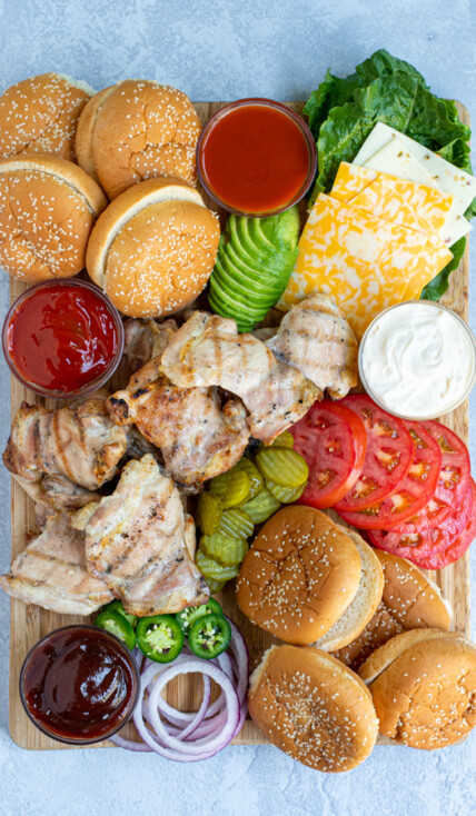 grilled chicken sandwich board filled with a variety of sauce, garnishes, buns, and grilled chicken
