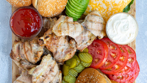 grilled chicken sandwich board filled with a variety of sauce, garnishes, buns, and grilled chicken