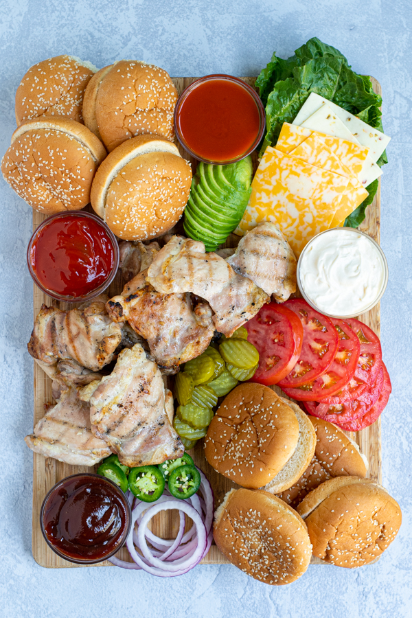 grilled chicken sandwich board filled with a variety of sauce, garnishes, buns, and grilled chicken