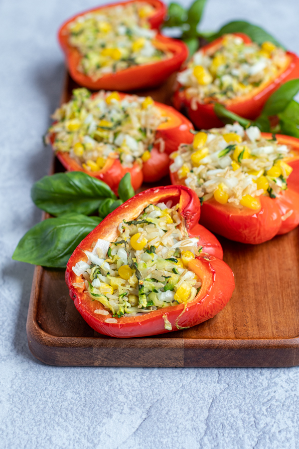 wood tray with grilled stuffed red bell peppers arranged next to fresh basil leaves