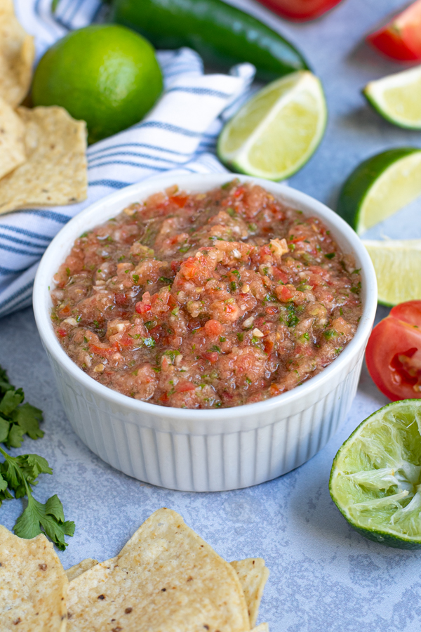 white bowl of freshly made salsa surrounded by tortilla chips and lime wedges