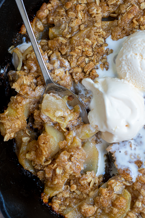 a large scoop of apple crisp in a serving spoon with melty vanilla ice cream