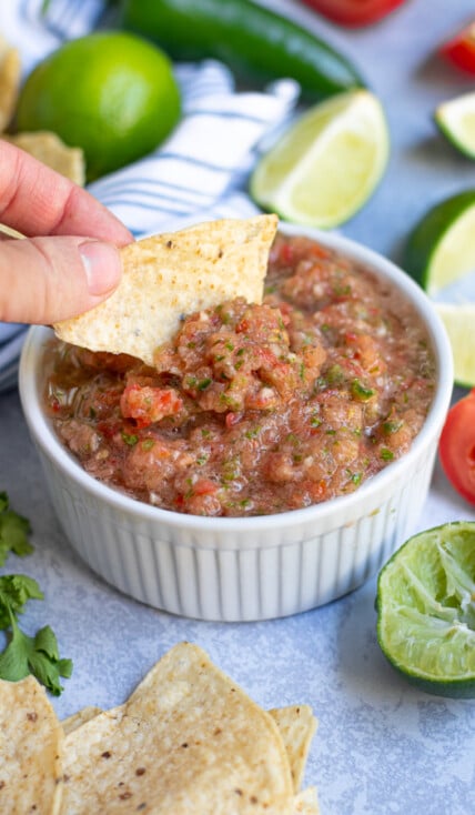 fresh restaurant style salsa being scooped out of a white bowl with a tortilla chip