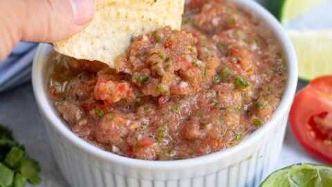 fresh restaurant style salsa being scooped out of a white bowl with a tortilla chip