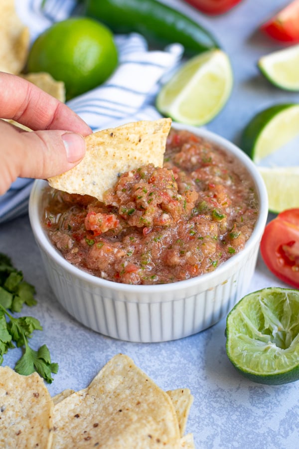 fresh restaurant style salsa being scooped out of a white bowl with a tortilla chip