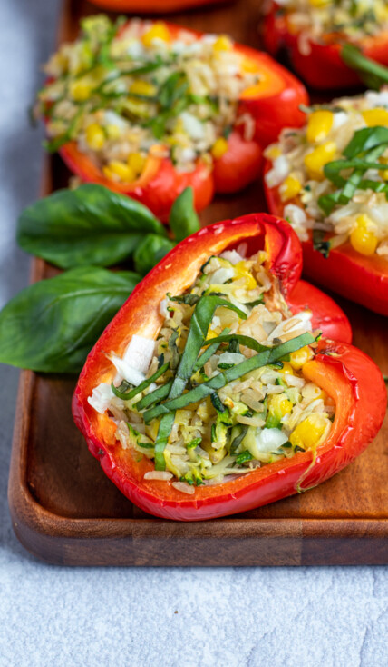 a close up of a grilled stuffed bell pepper topped with fresh basil leaves on a wooden serving tray