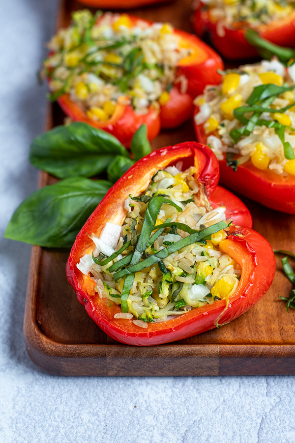 a close up of a grilled stuffed bell pepper topped with fresh basil leaves on a wooden serving tray