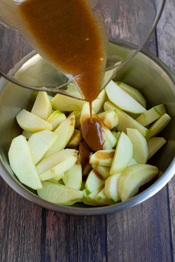 caramel colored filling being drizzled down over a bowl full of apple slices