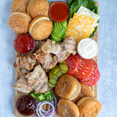 top view of a grilled chicken sandwich toppings board complete with grilled chicken, buns, and a variety of toppings